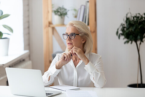 Woman in glasses in front of laptop looking out window